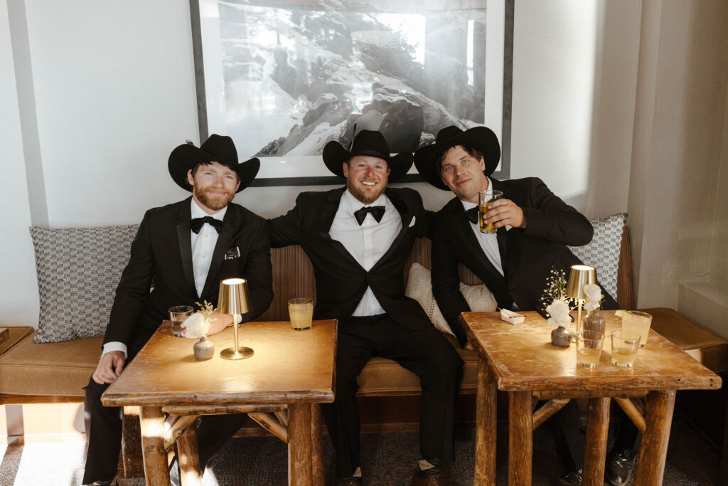 Groomsmen sitting on couch together smiling at camera with wooden tables in front of them at Heavenly Lake View Lodge