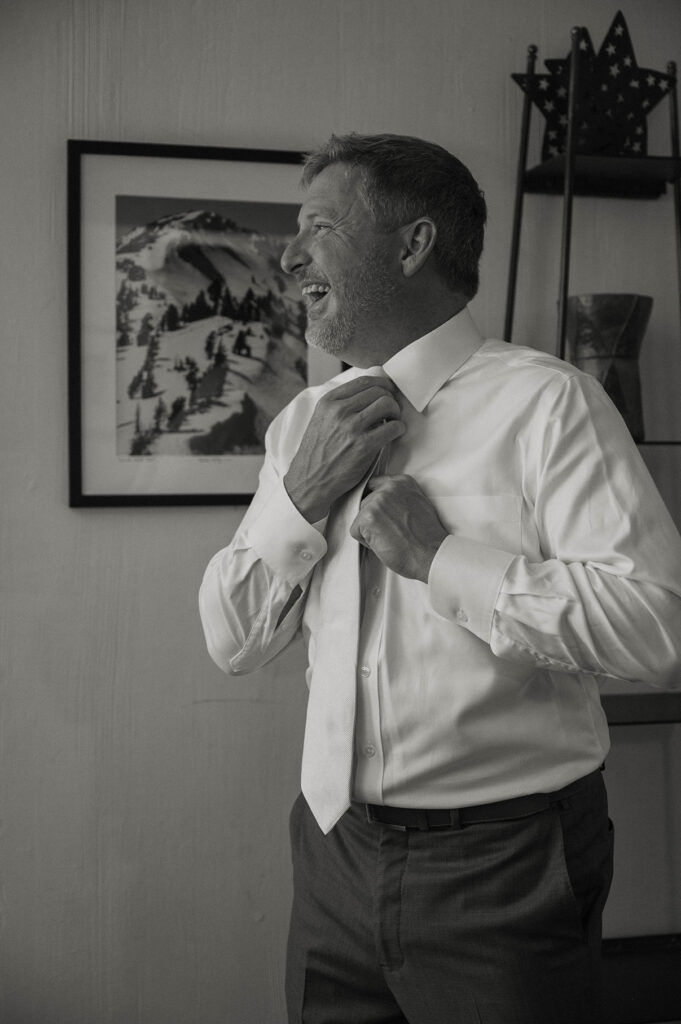 Wedding groom laughing while adjusting tie inside at PlumpJack Inn