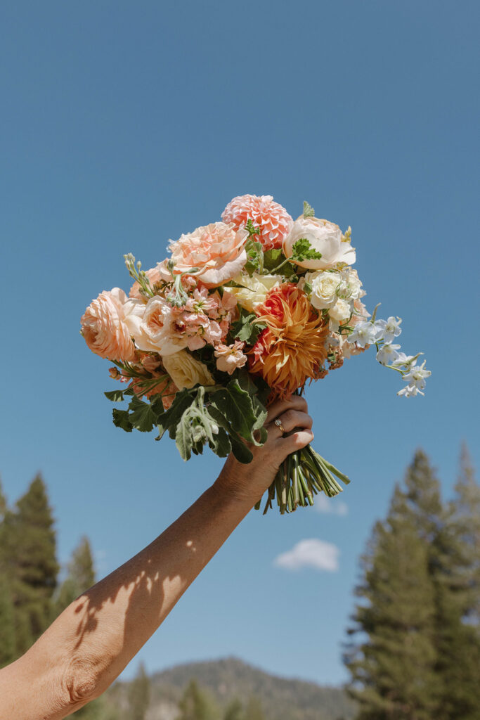 Bride holding colorful floral bouquet up in the air at PlumpJack Inn