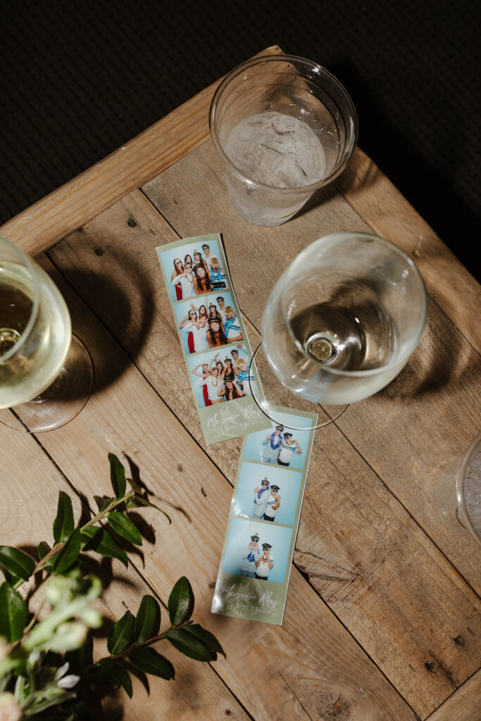 Photobooth photos on wooden table next to drink glasses and greenery