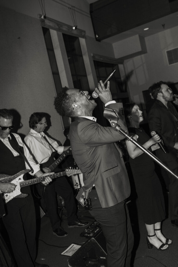 Singer singing into microphone while musicians play instruments behind him during wedding reception at the PlumpJack Inn