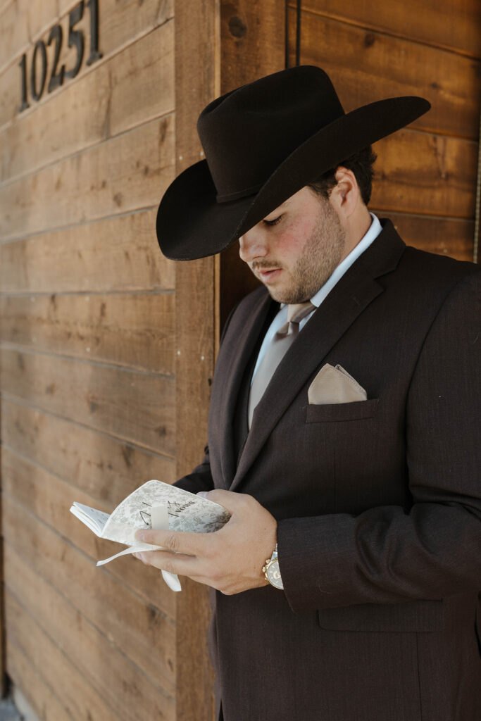 Groom leaning on all wooden building while reading wedding vow book at Austin Ridge Truckee