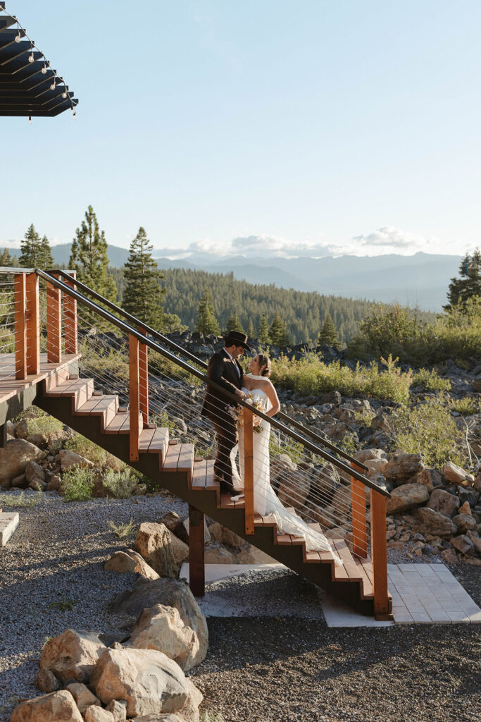 Wedding couple holding and looking at each other while standing on wooden staircase at Austin Ridge Truckee with forest of pine trees in background