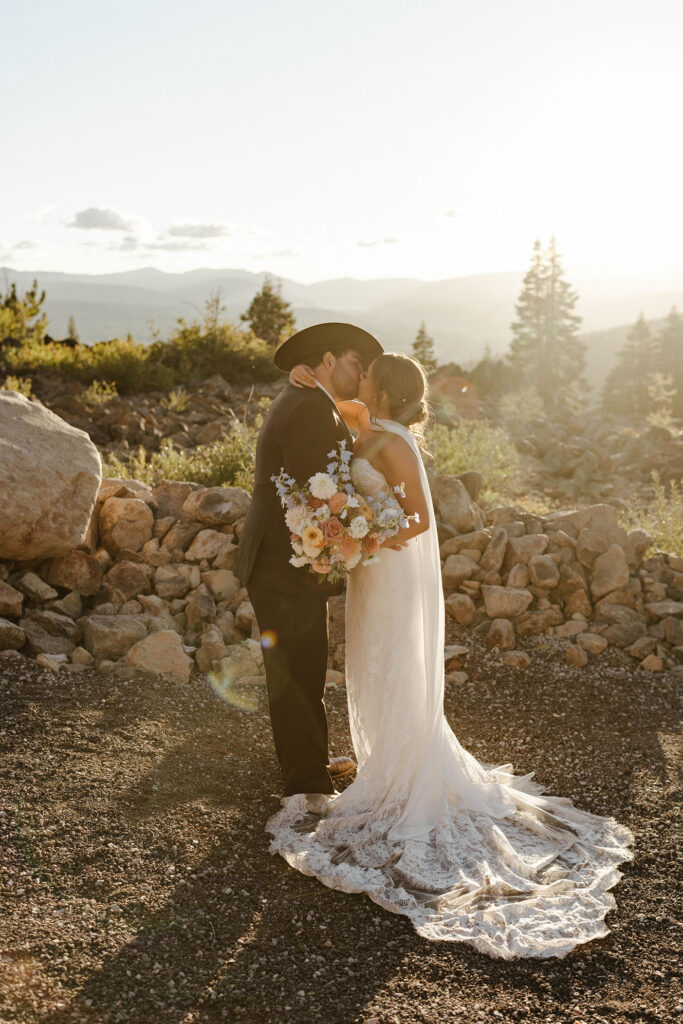 Wedding couple kissing in front of rocks while bride holds colorful floral bouquet during sunset at Austin Ridge Truckee