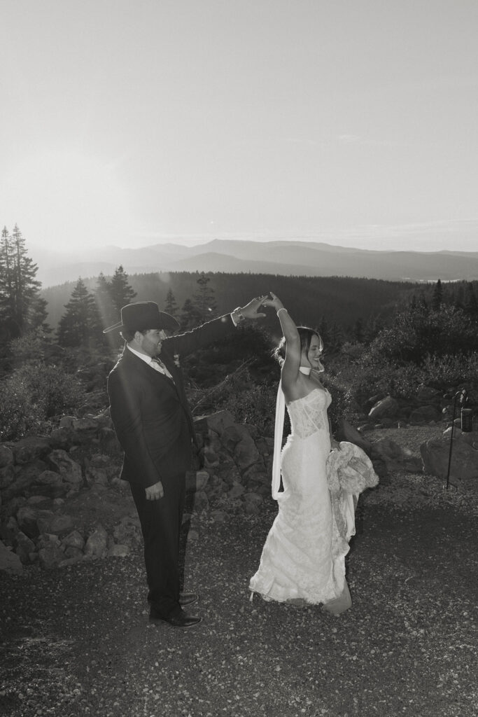Groom twirling wedding bride around while holding her hand at Austin Ridge Truckee with pine trees and shrubs in background
