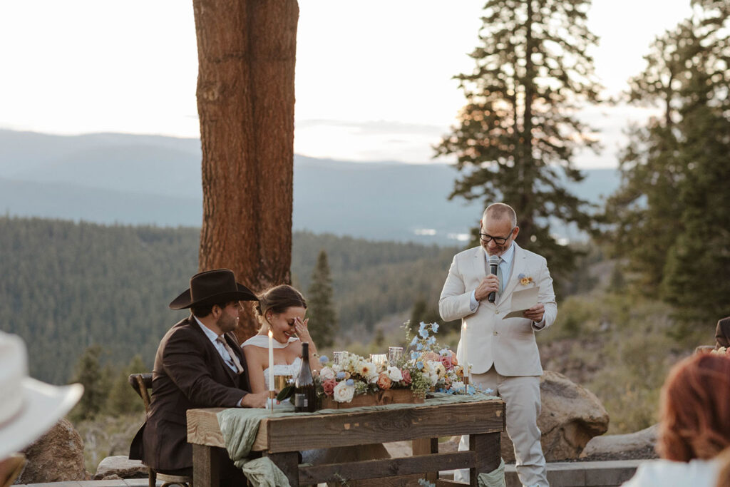 Bride's dad giving speech while bride is embarrassed during wedding reception at Austin Ridge Truckee with lots of pine trees in background