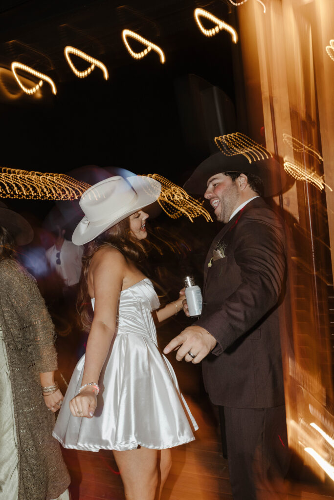Wedding couple dancing together while holding drinks during reception at Austin Ridge Truckee while lights blur around them