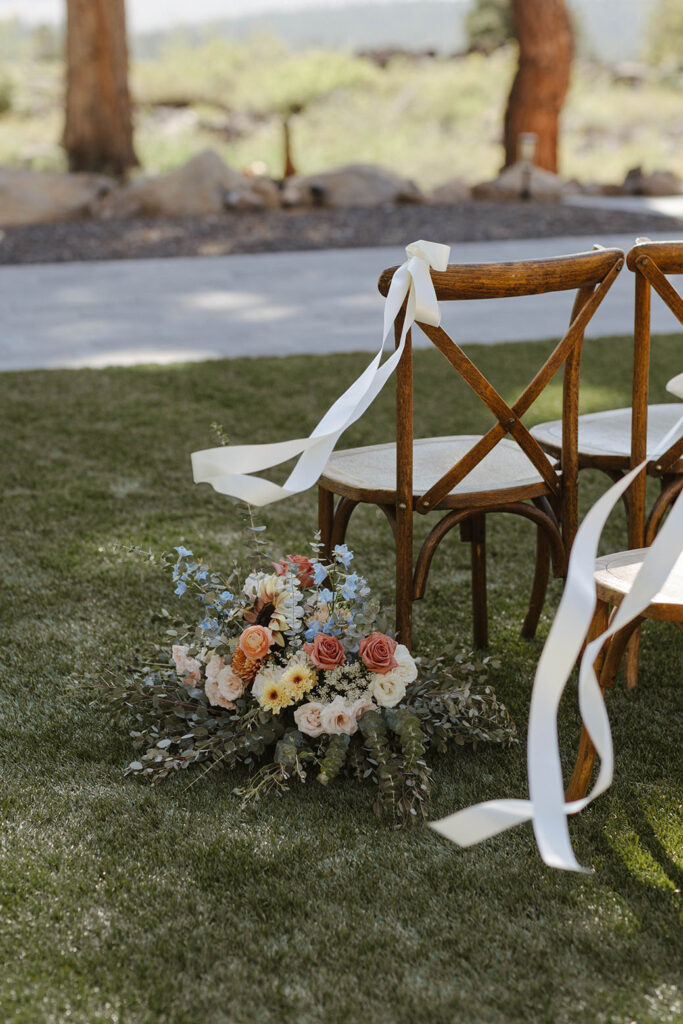 Colorful floral display sitting on grass next to wooden chairs with white ribbons at Austin Ridge Truckee