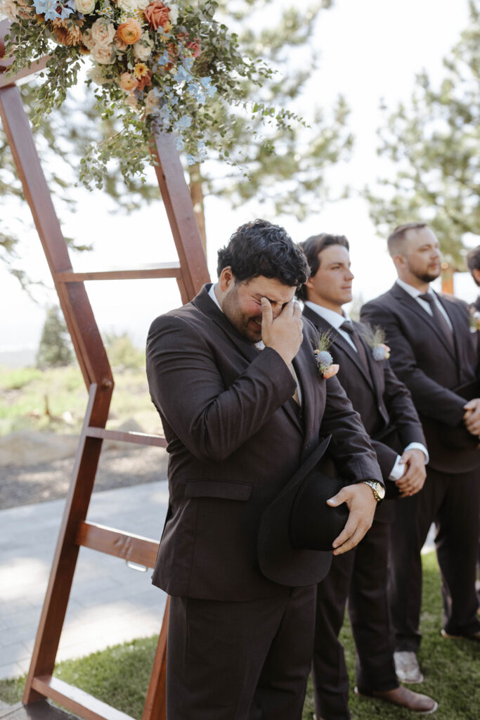 Groom emotional watching bride walk down wedding aisle to ceremony at Austin Ridge Truckee with groomsmen and wooden arch in background