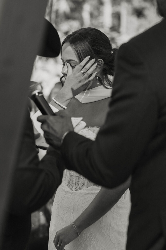 Bride wiping tears while listening to groom read wedding vows during ceremony at Austin Ridge Truckee