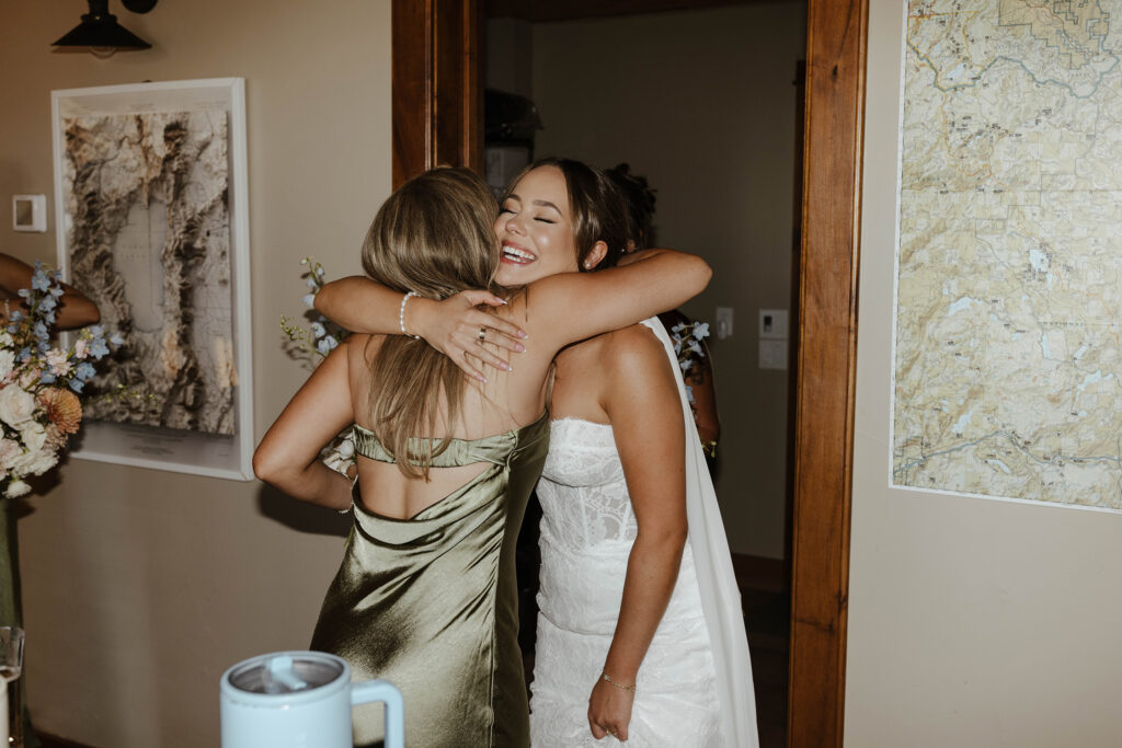 Wedding bride smiling while hugging bridesmaid inside at Austin Ridge Truckee