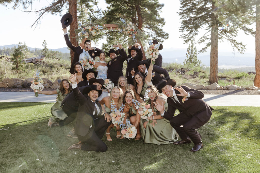 Bridal party posing with wedding couple and celebrating in front of wooden wedding arch at Austin Ridge Truckee with pine trees and greenery in background