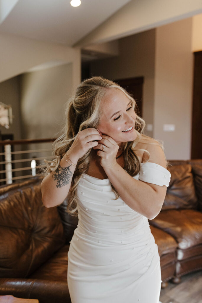 Elopement bride inside putting earring on while wearing wedding dress and smiling in Lake Tahoe