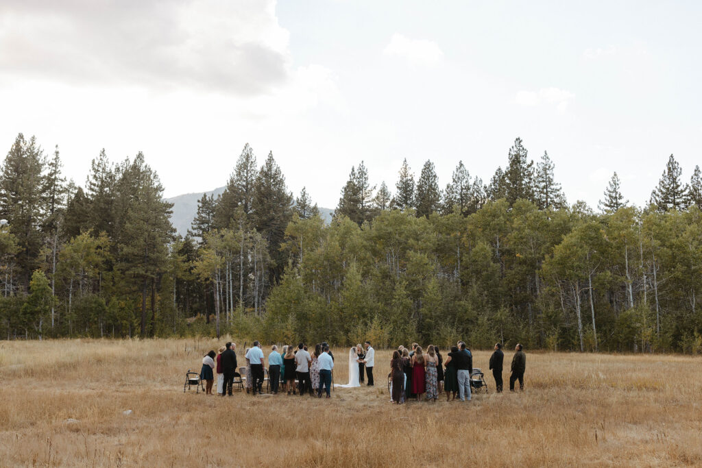 Overview of elopement ceremony with guests standing and watching on both sides of the couple and lots of pine trees in background at Lake Tahoe