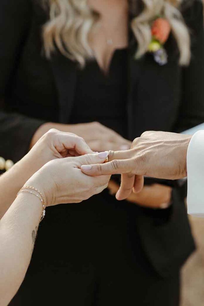 Close up of bride sliding wedding ring onto groom's finger during elopement ceremony at Lake Tahoe