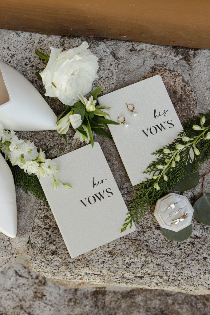 His and hers vow books sitting on rocks next to white floral decor and wedding rings at Valhalla Tahoe