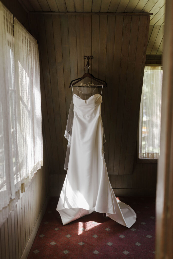 Silk wedding dress on wooden hanger in front of dark wooden wall at Valhalla