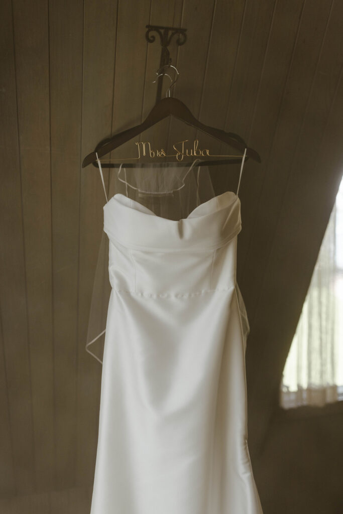 Wedding dress hanging on wooden hanger with brides new last name spelled out in wire at Valhalla Tahoe
