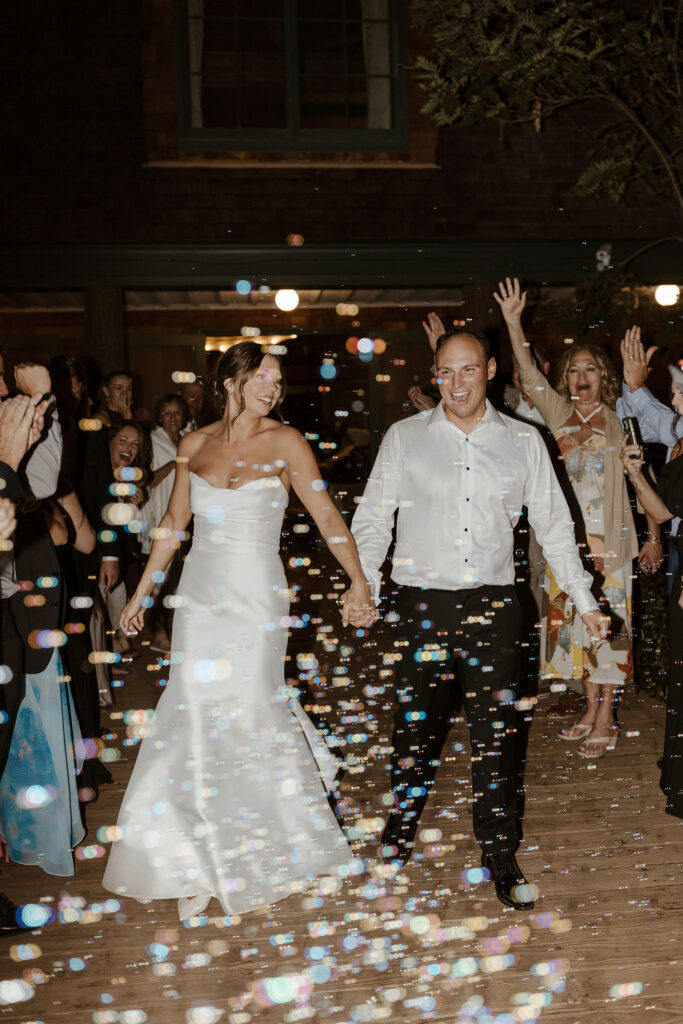 Wedding couple holding hands and laughing while guests blow bubbles all around them and celebrate at Valhalla Tahoe