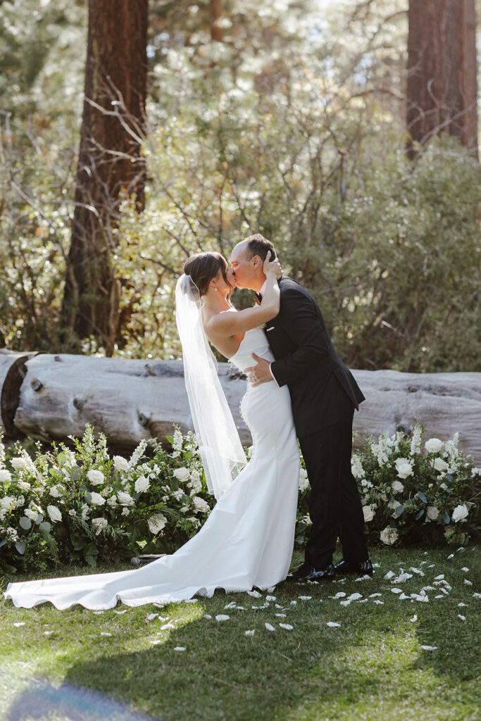 Wedding couple's first kiss after ceremony at Valhalla Tahoe in front of white flowers and greenery