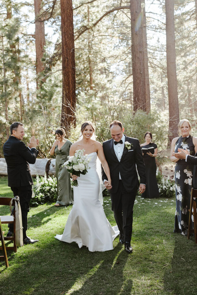Wedding couple holding hands and walking down aisle together after ceremony with guests clapping on either side at Valhalla Tahoe