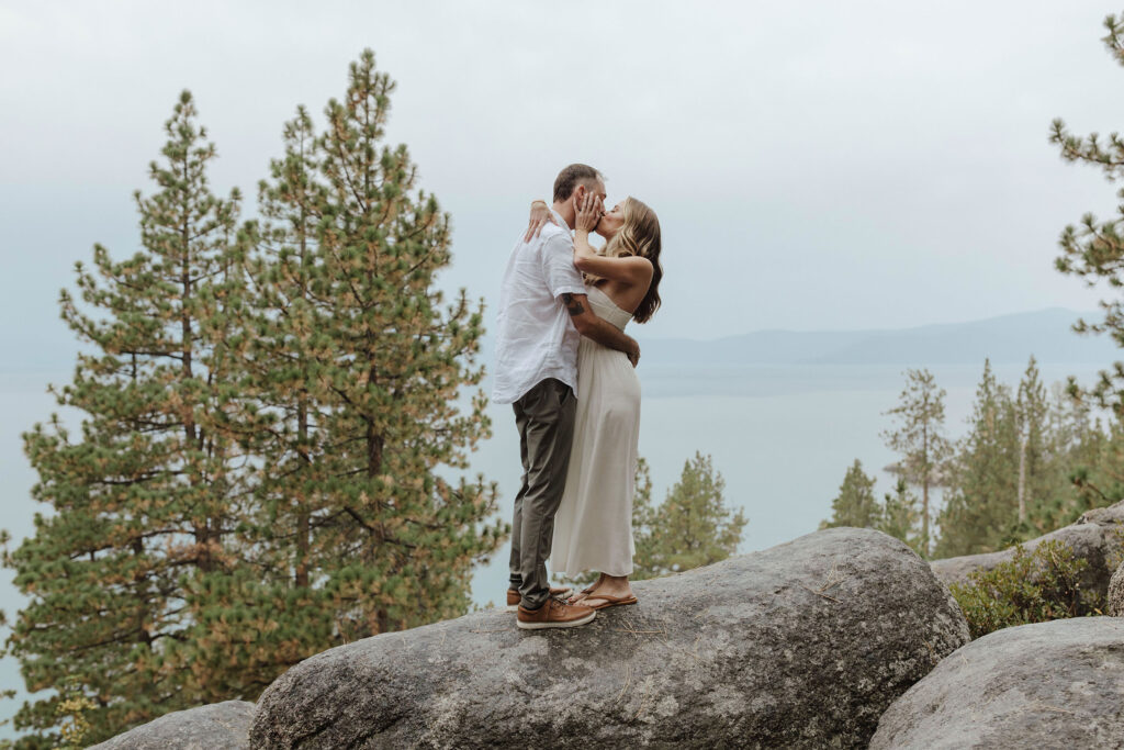 engagement couple standing on a rock in lake tahoe kissing in the rain