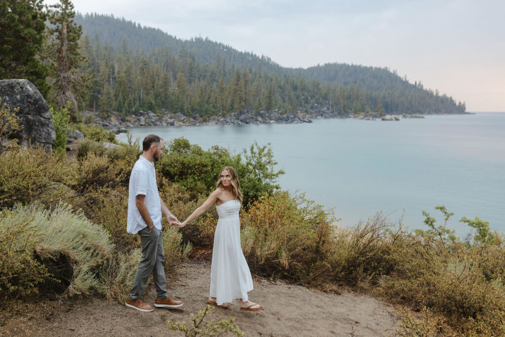 woman looking back at the man holding his hand taking engagement photos in the rain in lake tahoe with the lake in the background