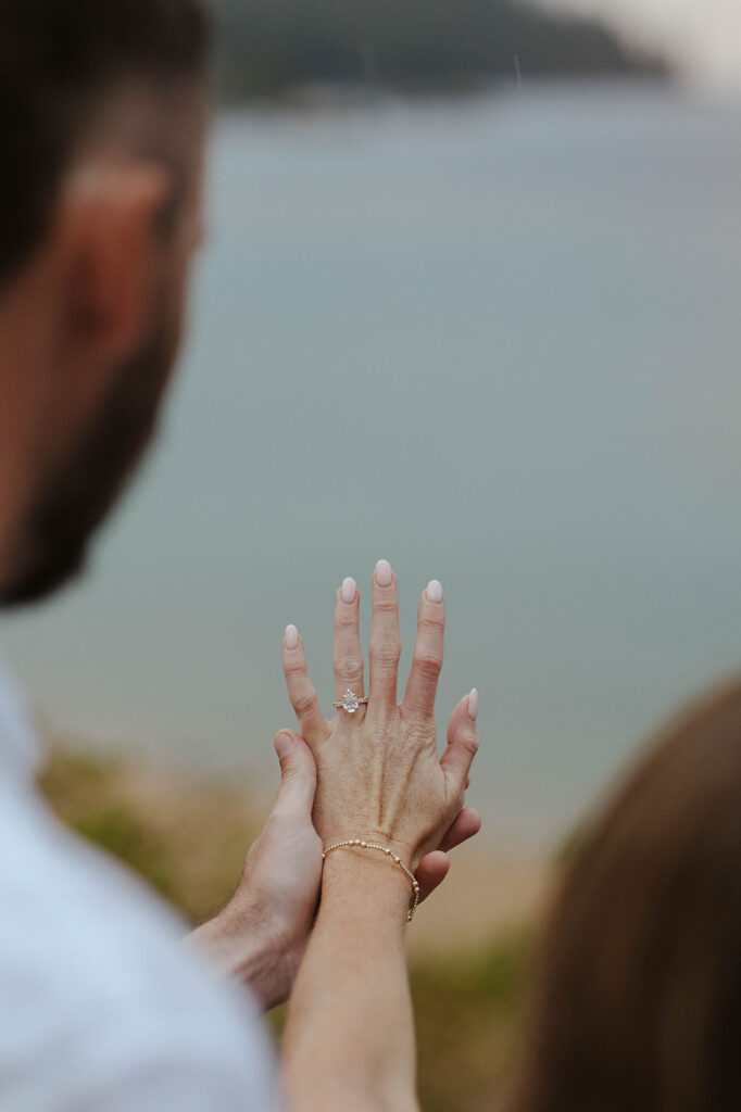 woman holding out her left hand showing engagement ring while man holds her hand in lake tahoe
