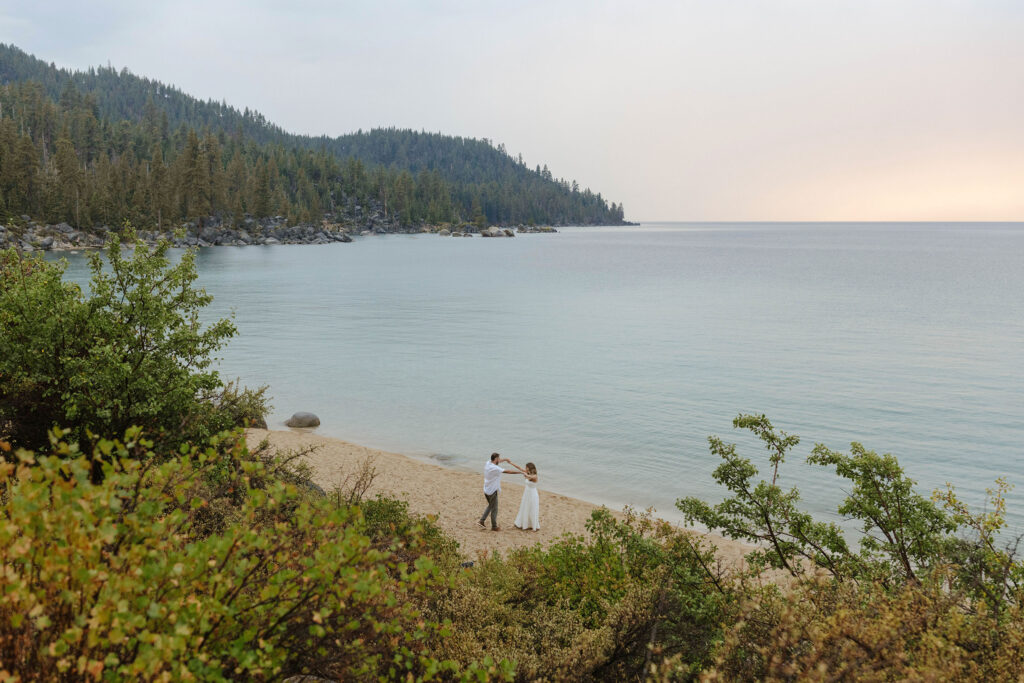 landscape view of lake tahoe taking engagement photos while couple dances on the beach in the rain 