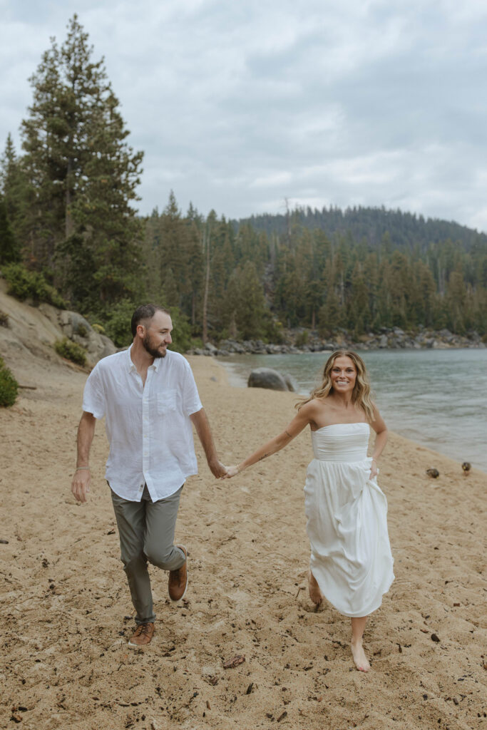 engagement couple running on the beach in lake tahoe laughing while it rains