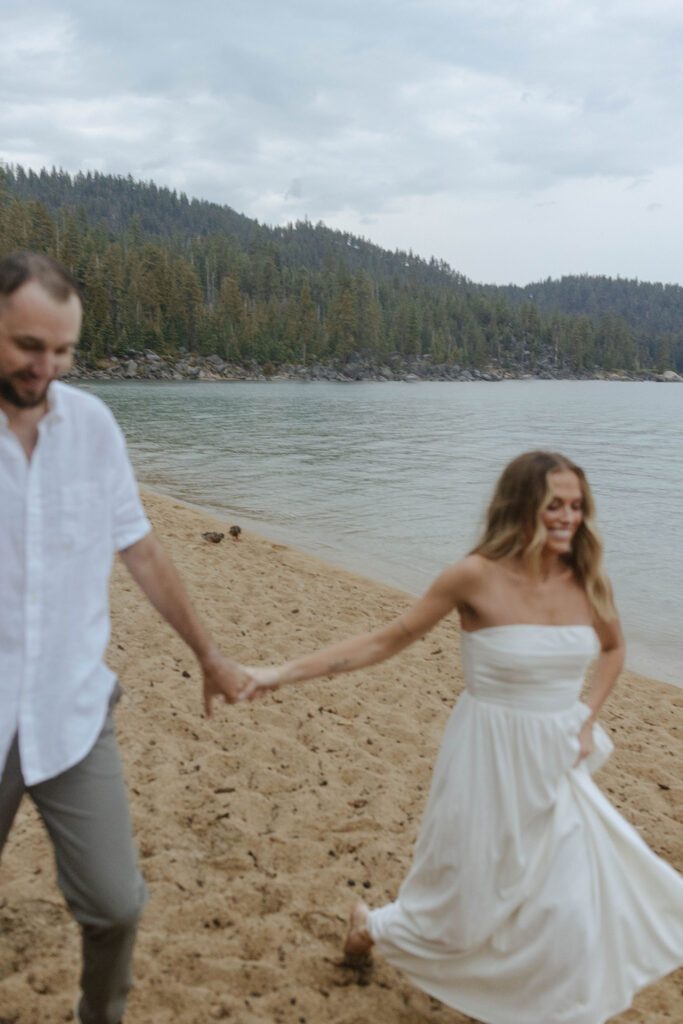 couple running on the sand in the rain in lake tahoe for their engagement photos with the lake in focus