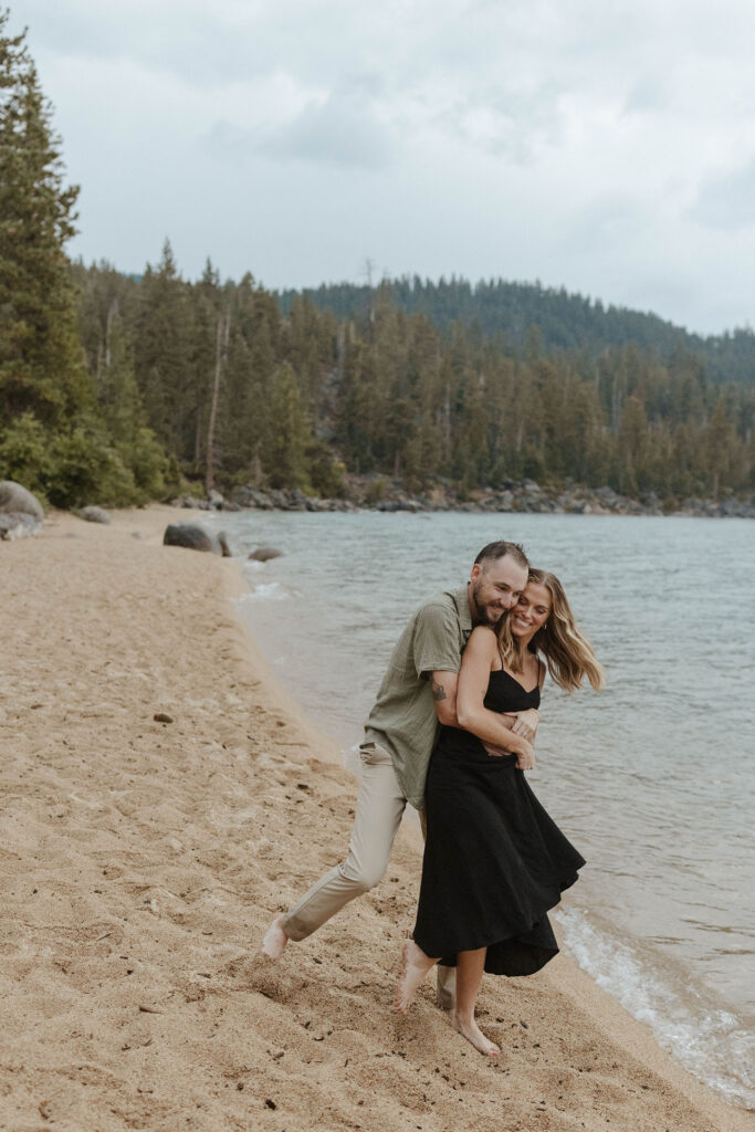 man hugging woman from behind while she laughs on a beach in lake tahoe