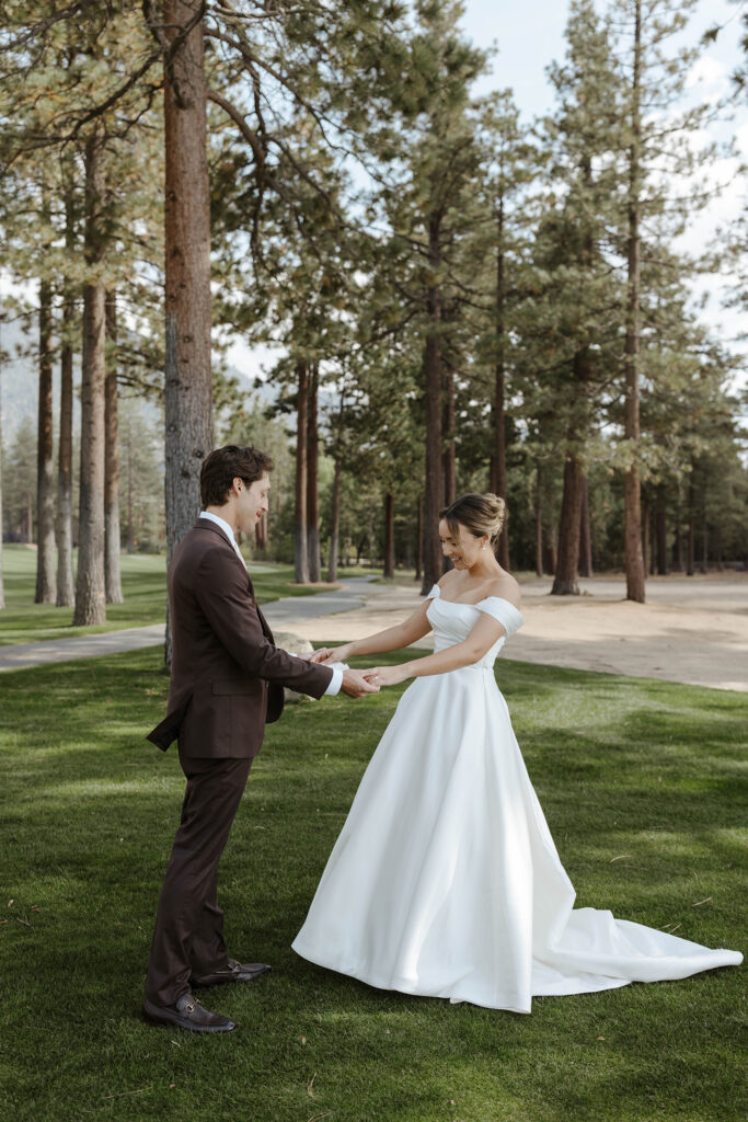 Wedding couple holding hands while standing in grass together in front of large pine trees at Edgewood Tahoe
