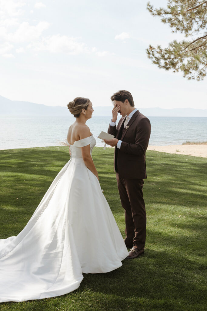 Groom emotional while reading wedding vows from vow book to bride at Edgewood with Lake Tahoe in background