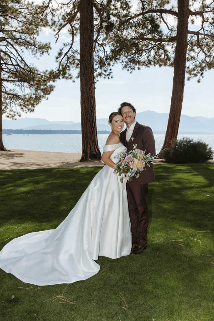 Wedding couple standing together and smiling at camera with pine trees and Lake Tahoe in background at Edgewood