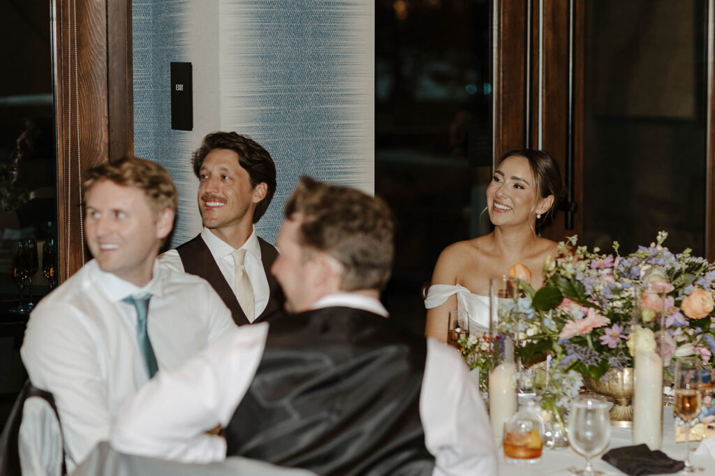 Wedding couple sitting at reception table together with colorful floral decorations and listening to speeches at Edgewood Tahoe