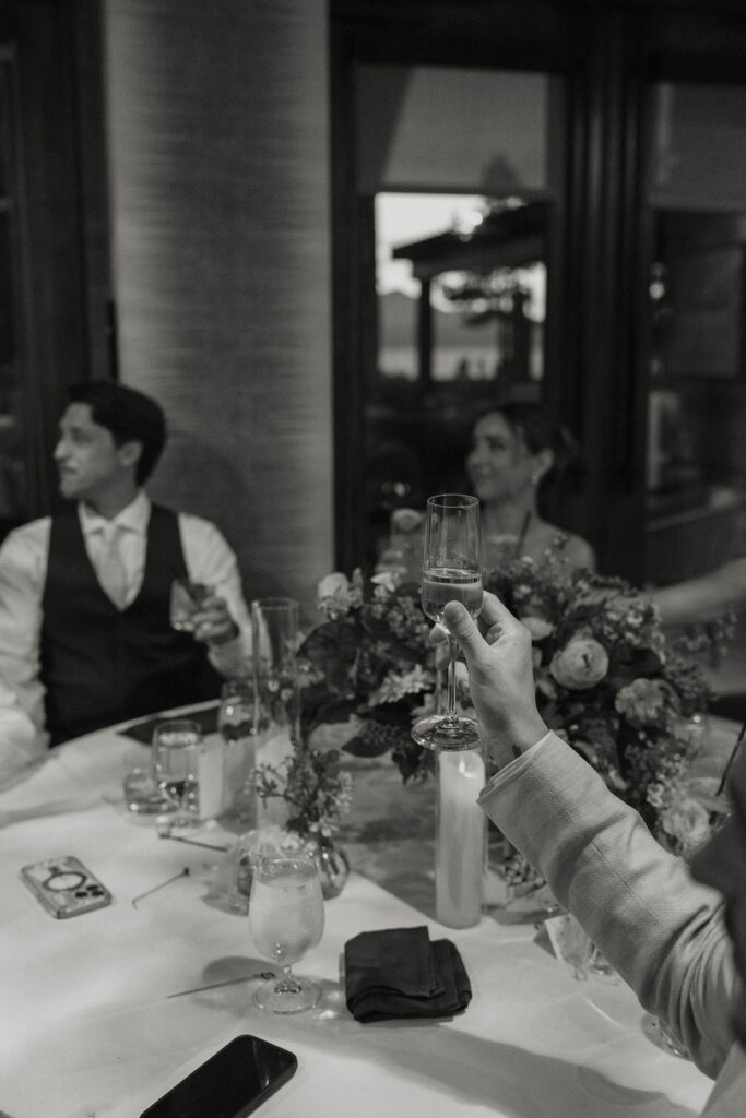 Close up of guest holding champagne glass in the air to toast during reception at Edgewood Tahoe with wedding couple in background