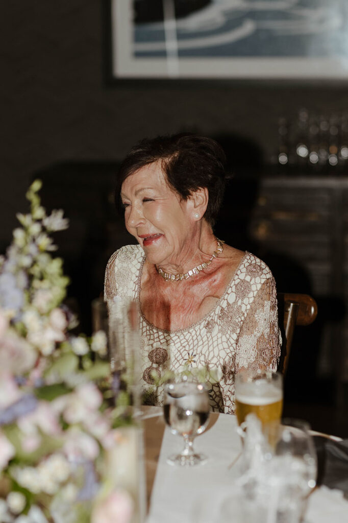 Wedding guest laughing while sitting at reception table decorated with colorful florals and drinks at Edgewood Tahoe