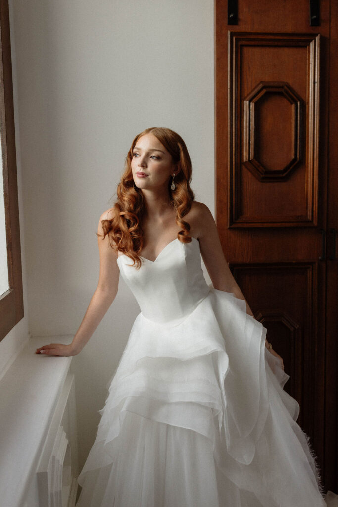 Bride in a strapless wedding dress standing by a window during getting ready photos on a Lake Tahoe wedding day