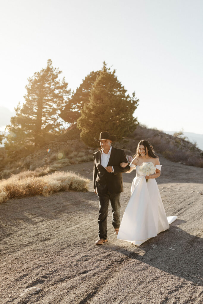 Bride holding dad's arm and walking down trail to elopement ceremony in Lake Tahoe