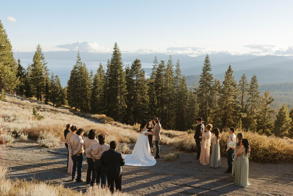 Overview of elopement ceremony with guests on either side with tall pine trees and Lake Tahoe in background