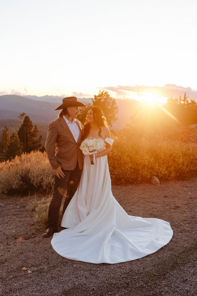 Elopement couple holding each other and smiling on trail next to yellow bushes with sunset in background in Lake Tahoe