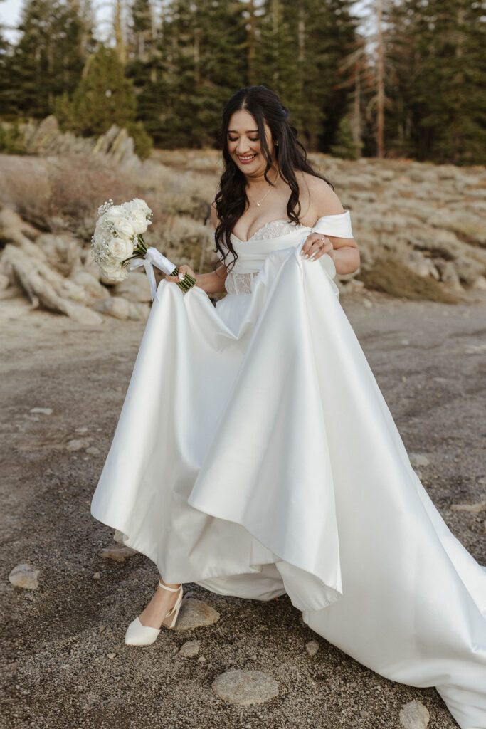 Elopement bride holding floral bouquet and dress while walking down trail and smiling in Lake Tahoe