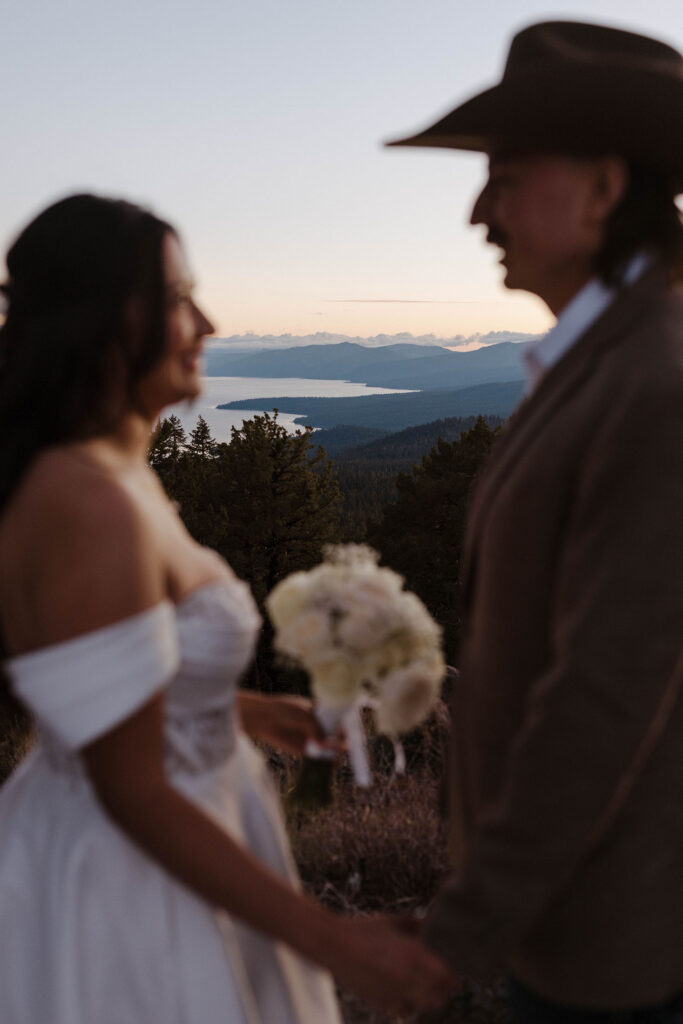 Close up of elopement couple holding hands and looking at each other with Lake Tahoe in between them in background