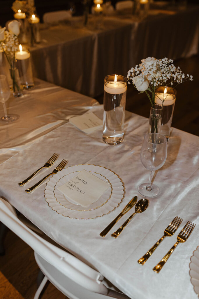 Elopement reception table with white and gold plates and gold cutlery next to candles and white florals