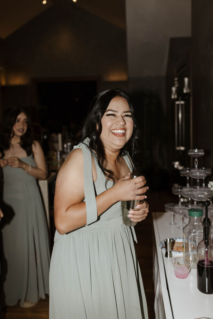 Wedding guest laughing while holding cup during elopement reception with guests in background