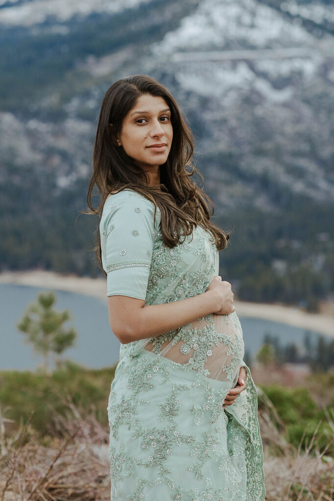 pregnant woman looking at the camera holding her belly in a teal blue dress for her tahoe maternity photos