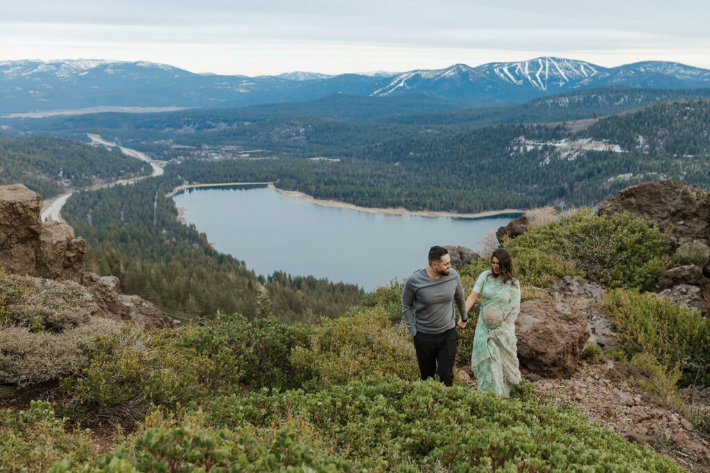 maternity couple holding hands smiling and walking with lake tahoe behind them 