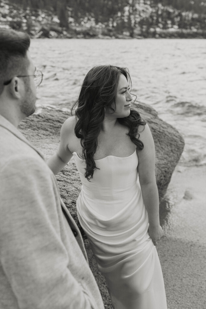 Woman looking out at Lake Tahoe while standing next to fiancé with large rock in background