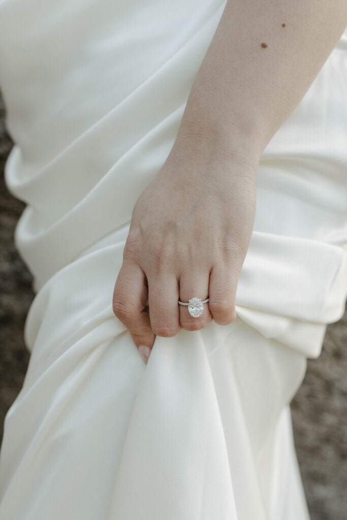 Close up of engagement ring on woman's finger while her hand holds her dress